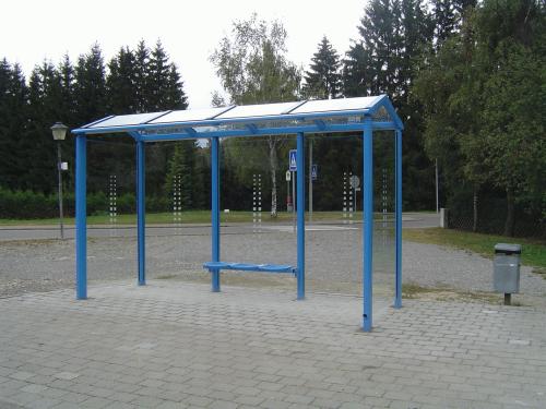 Eine Wartehalle am Wegesrand mit Drahtgittersitzen und Abfallbehälter