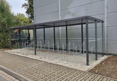 Eine Fahrradüberdachung mit mehreren Fahrradbügeln vor einer Metallwand