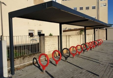 Eine Fahrradüberdachung mit mehreren runden Fahrradbügeln vor einer Steinmauer