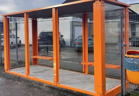 Ein orangefarbener Raucherunterstand mit drei Feldern und Drahtgittersitzen