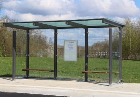 Eine graue dreifeldrige Wartehalle mit zwei Holzbänken und Scheibendekor