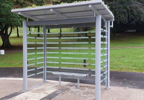 Eine graue Wartehalle mit Dachbegrünung am Wegesrand