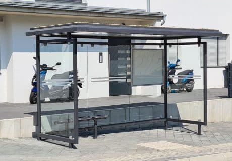 Eine graue Wartehalle mit Dachbegrünung am Straßenrand