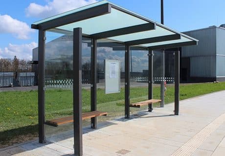 Eine graue dreifeldrige Wartehalle mit zwei Holzbänken und Fahrplanvitrine