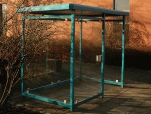 Ein weißer Raucherunterstand vor einer Steinmauer am Wegesrand