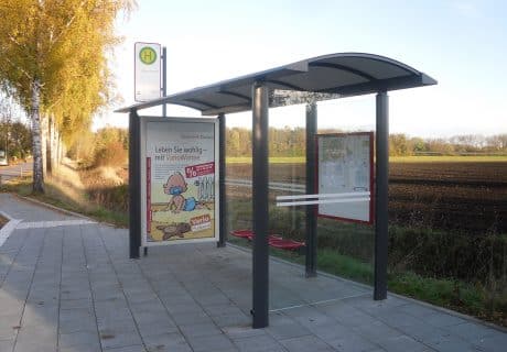 Eine graue Wartehalle mit Werbevitrine am Wegesrand